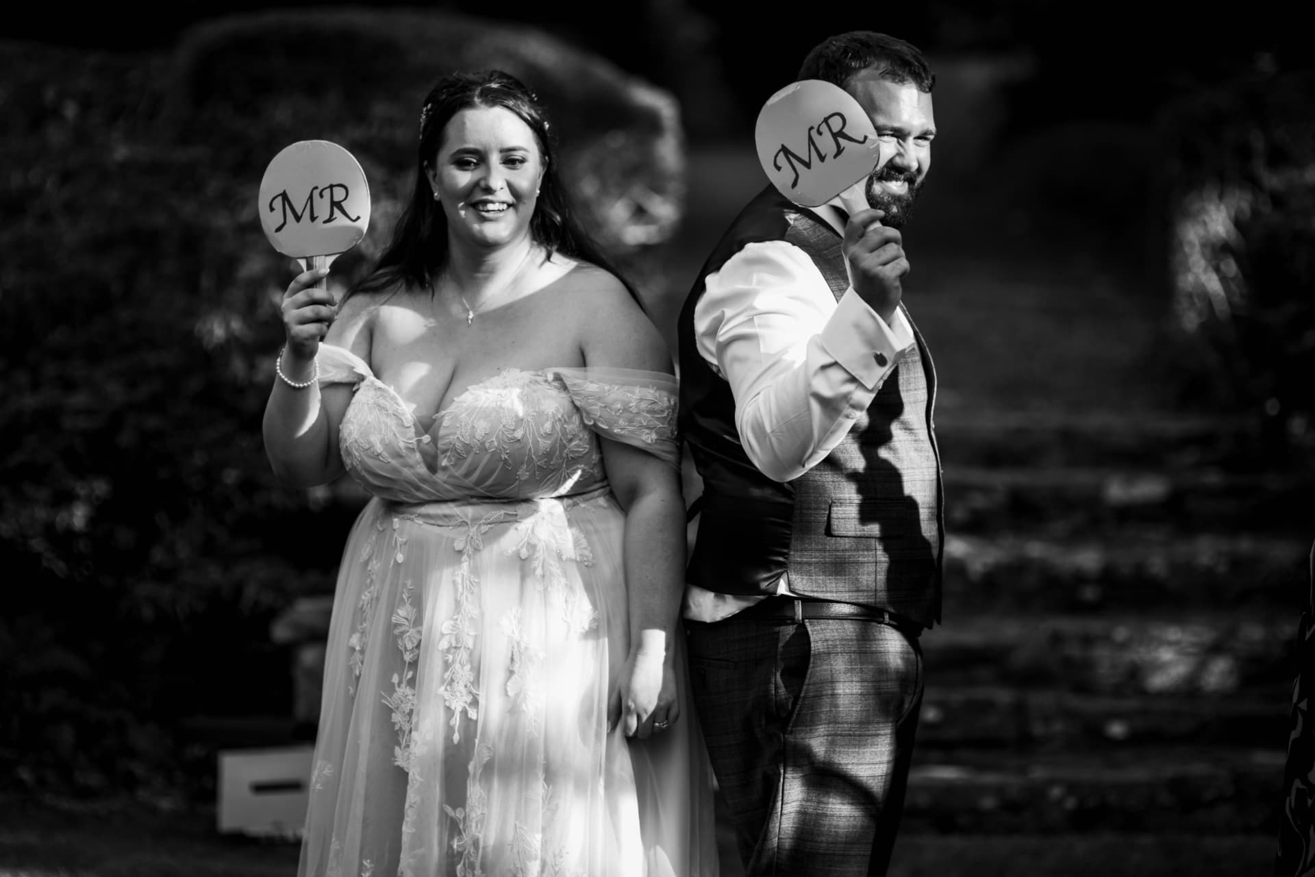 Bride and groom standing back to back holding up Mr paddles during a reception game, black and white
