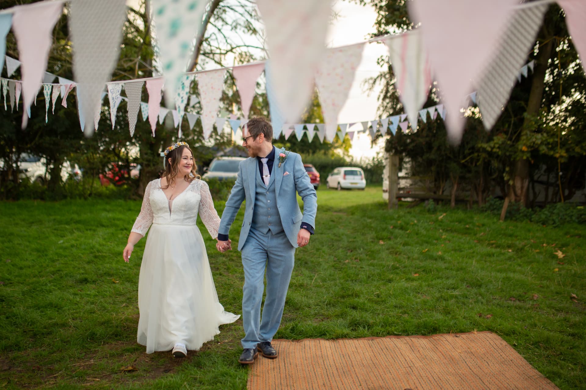 Bride and groom walking hand in hand across a lawn under pastel bunting