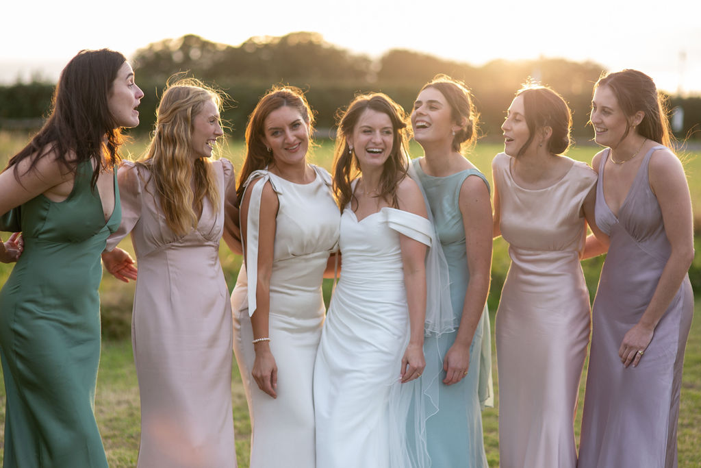 Bride laughing with her bridesmaids in a field at sunset