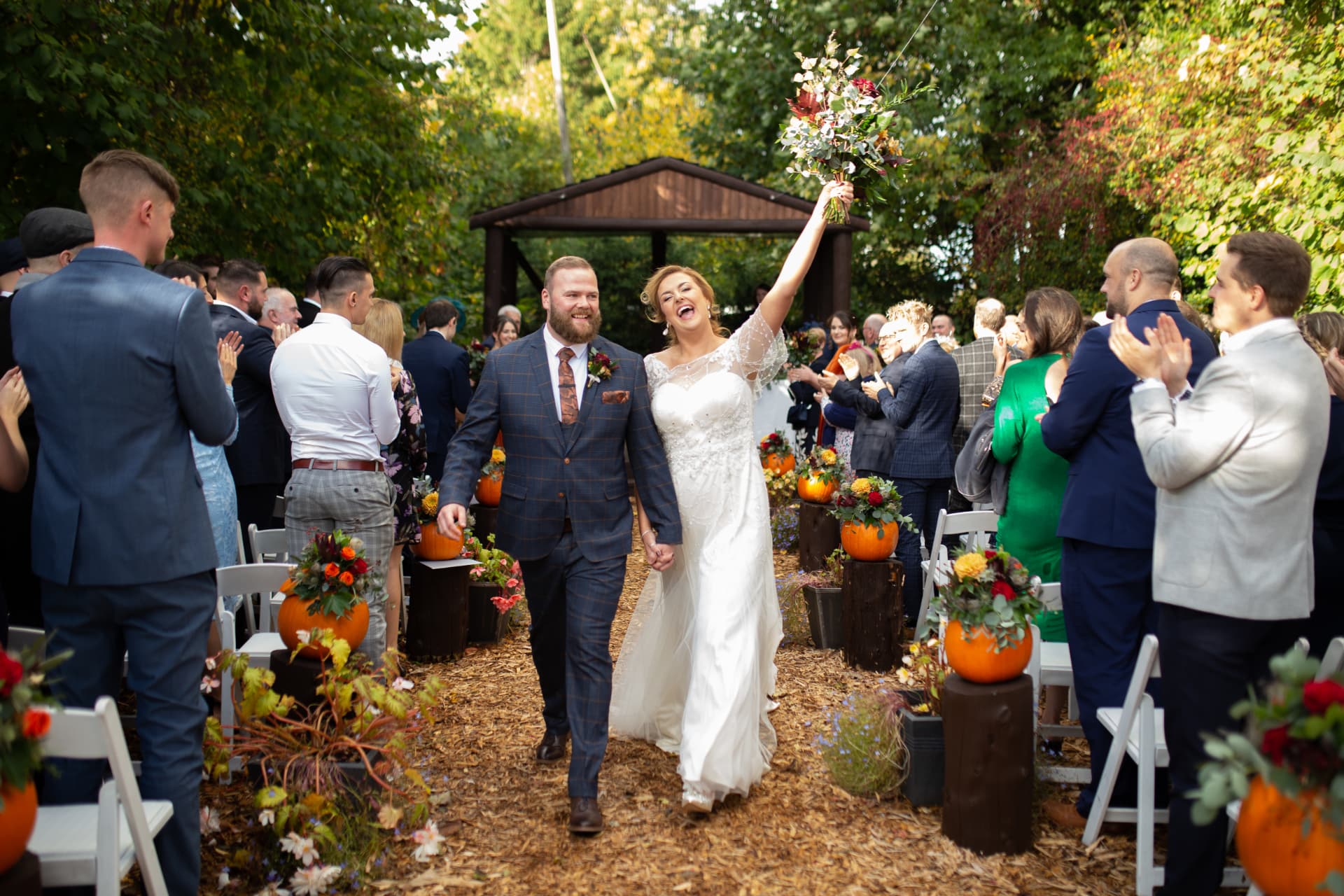 Bride and groom walking back down the aisle in autumn, bouquet raised