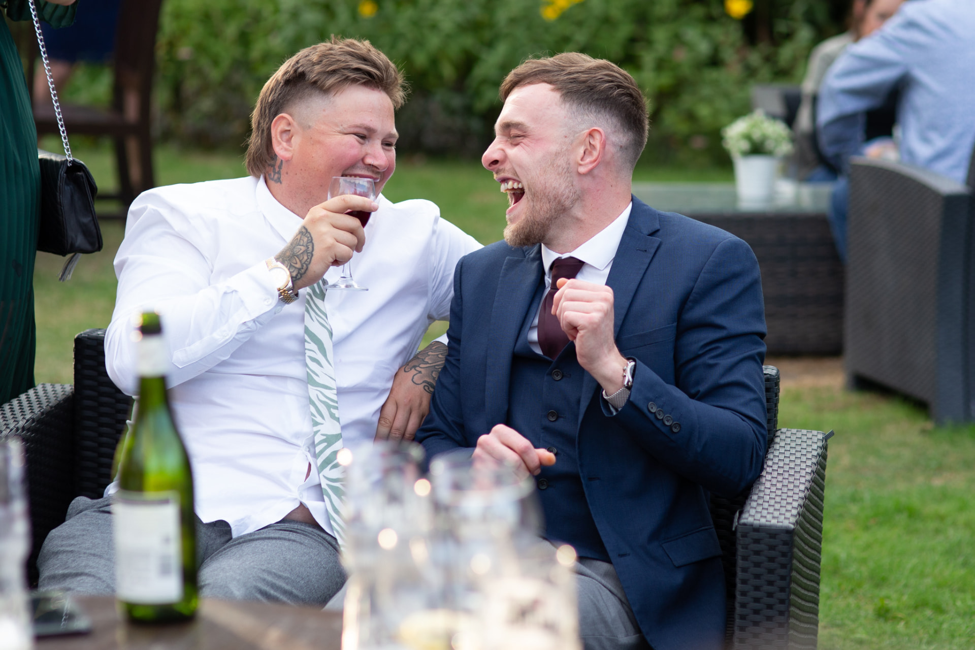 Two wedding guests laughing with drinks in their hands on the lawn