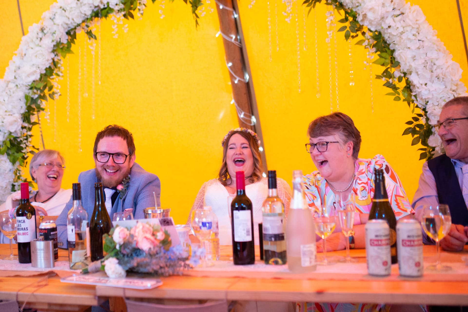 Five guests at the head table in fits of laughter under a yellow marquee