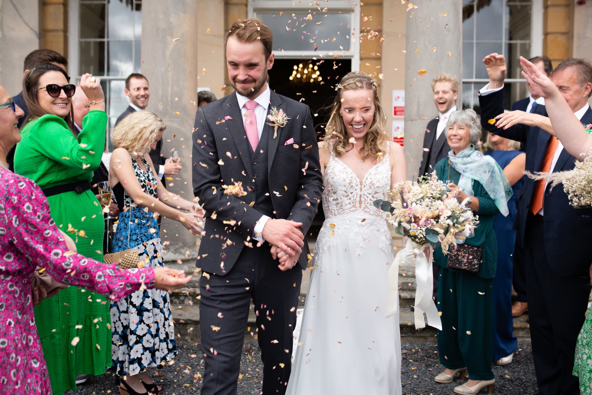 Couple walking through a shower of petal confetti outside a grand house