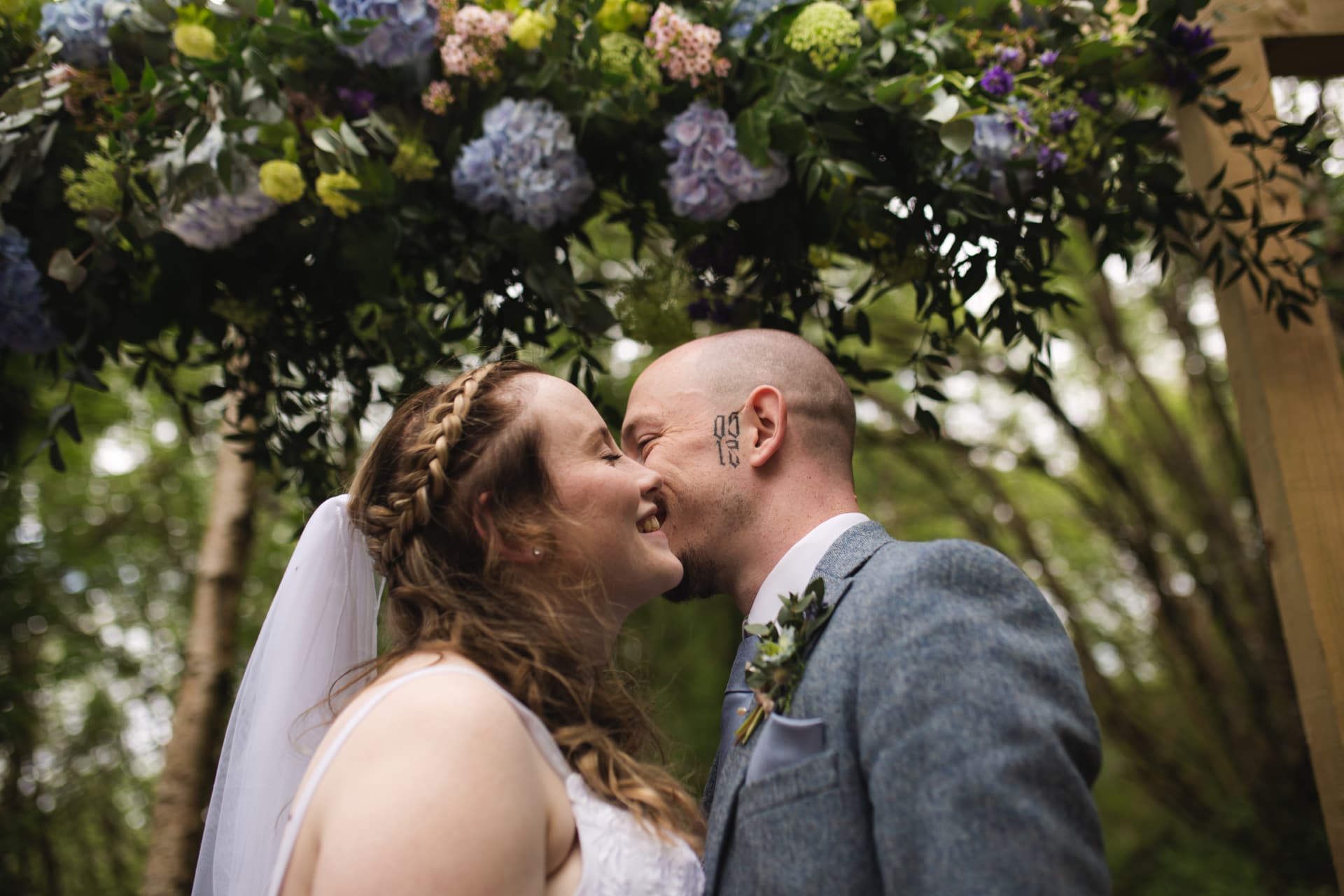 Bride and groom kissing under a floral arch in the woods