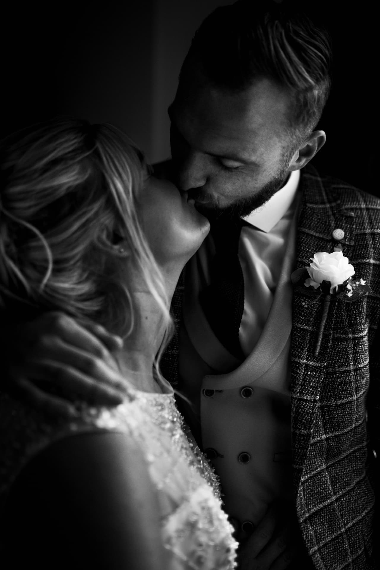 Dramatic low-light black and white kiss, groom's hand cradling the bride's head