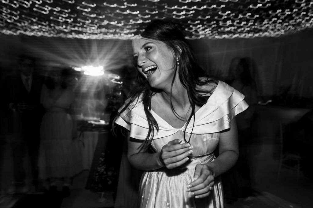 Wedding guest laughing and dancing on a dance floor under fairy lights, black and white