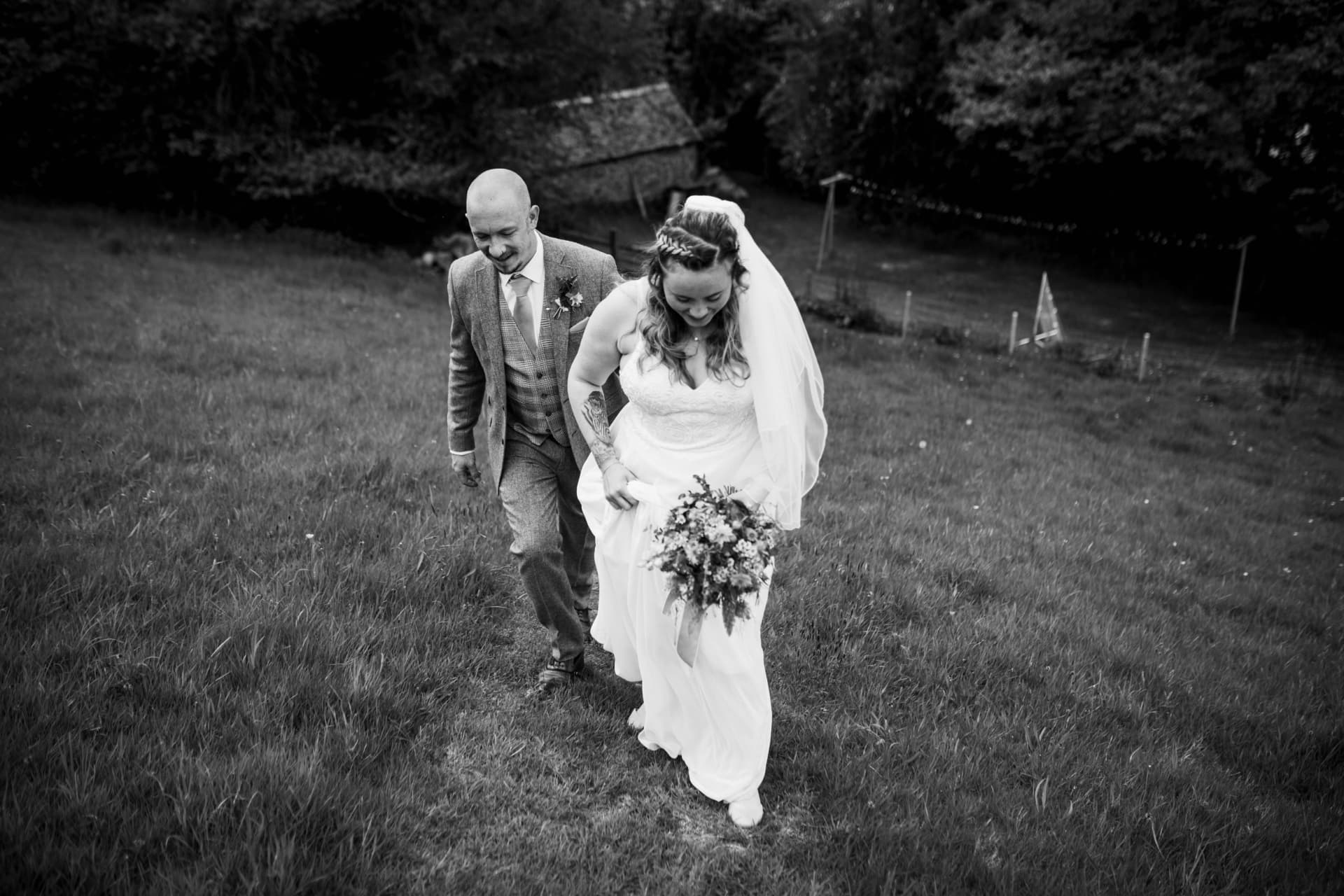 Bride and groom climbing a grassy hill, black and white